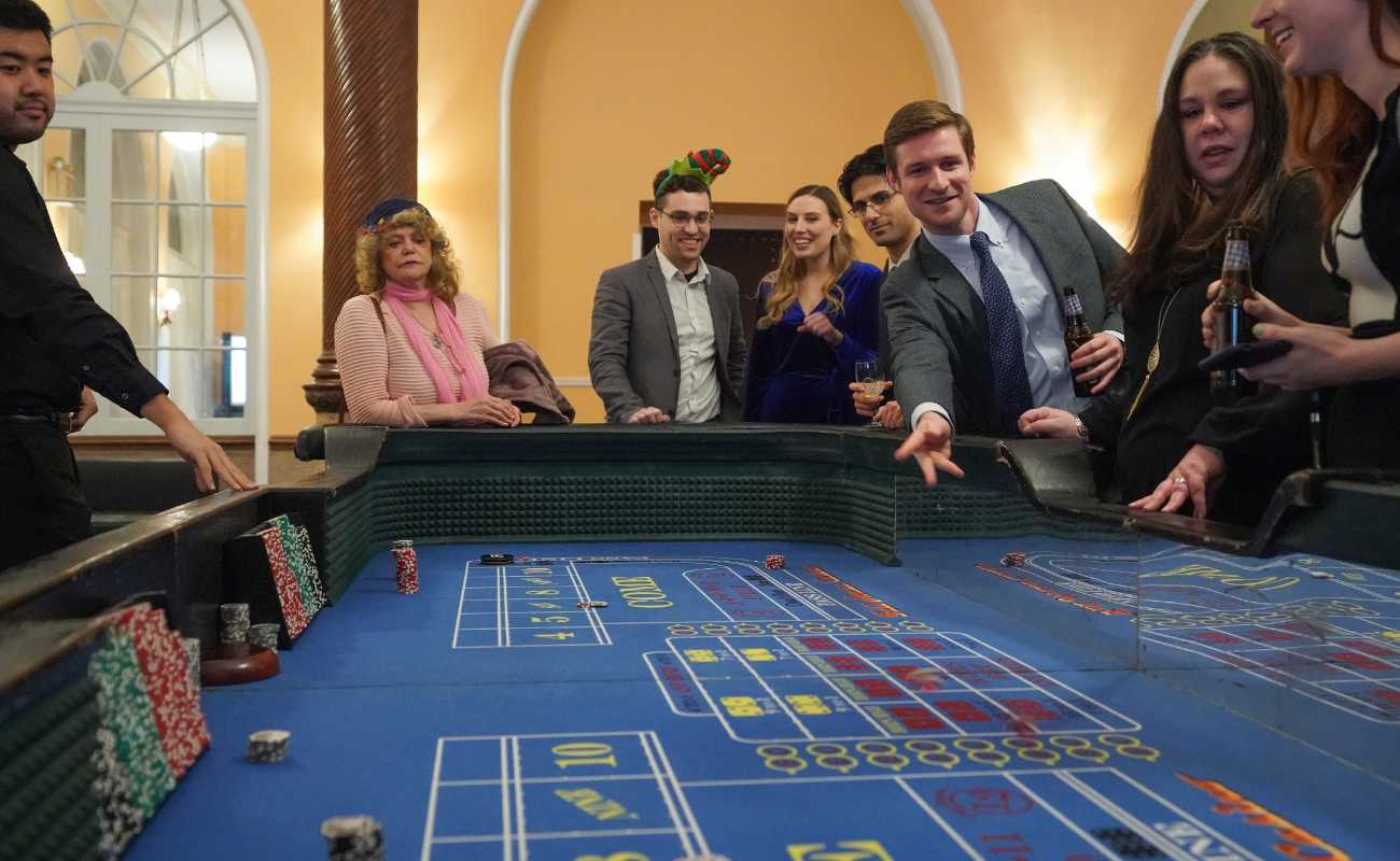 Man rolls and throws the dice during a game of craps, while people around the table watch