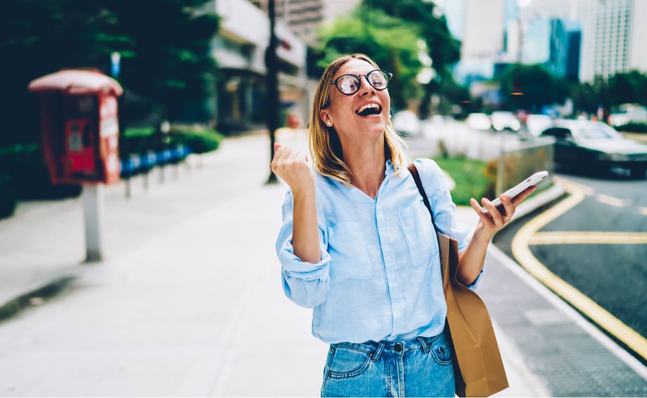 Young women wearing glasses, celebrating with a cellphone in her hand