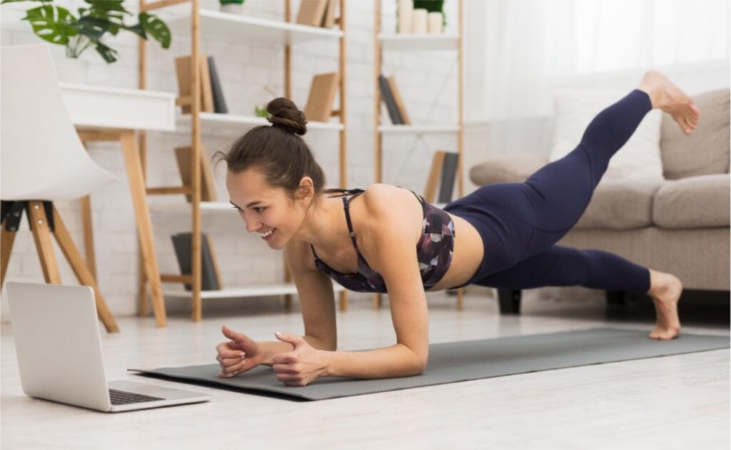 Fit woman doing yoga plank and watching online tutorials on laptop in living room