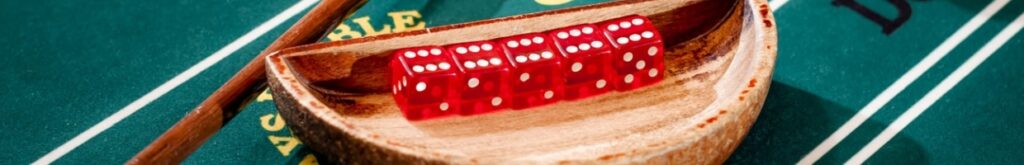 Full set of 5 dice in a wooden bowl next to the stick on a craps table with stacks of casino chip around