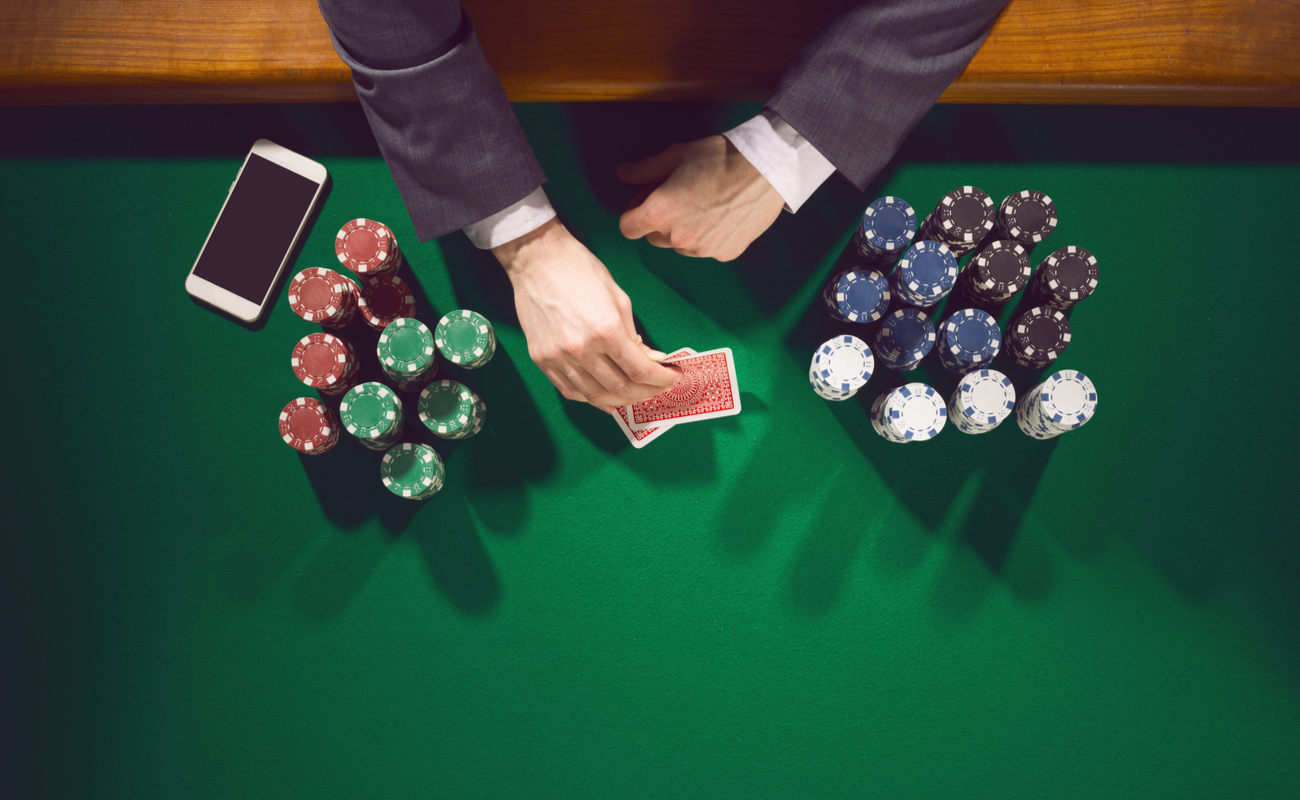 Hands holding cards with casino chips and a smartphone on a green casino table.