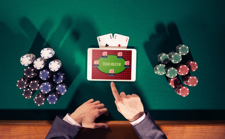 Poker player’s hand with a tablet and stacks of casino chips on a green felt casino table.