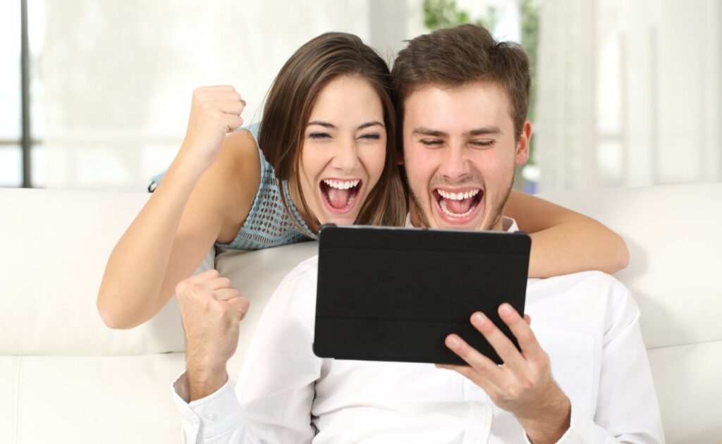 A young couple celebrates their online win while playing on a tablet.