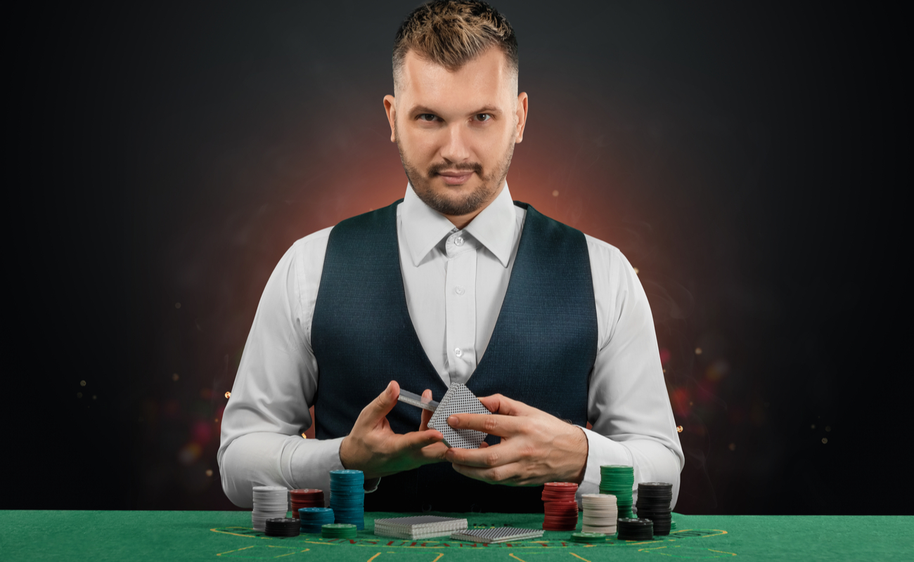 A dealer in a white shirt and dark waistcoat, shuffling cards at a casino table.