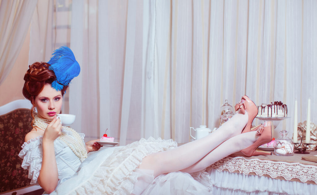 A woman drinking tea with her feet on the table, wearing a Marie-Antoinette-style dress.