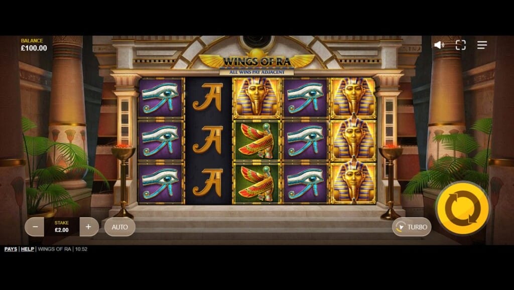 A screenshot of the reels from the Wings of Ra slot game. It displays a stately Egyptian temple interior with tall columns, burning coal stands, and lush green palms flanking the ornate golden reel structure. The game reels are filled with thematic symbols, including pharaoh masks, the Eye of Horus, Nefertiti busts, and traditional card icons like K and Q, all displayed against rich, textured backgrounds. The golden Wings of Ra title and radiant sun emblem sit at the top center, carved into the temple's architecture. Glowing braziers and soft ambient lighting enhance the immersive, regal atmosphere.