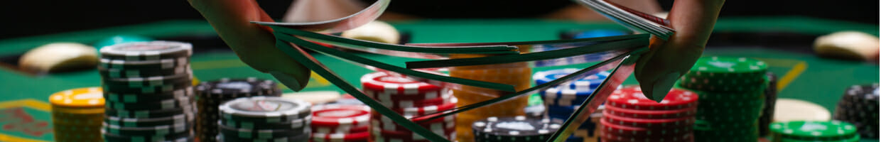 Close-up of a poker dealer shuffling cards with casino chips in the background.