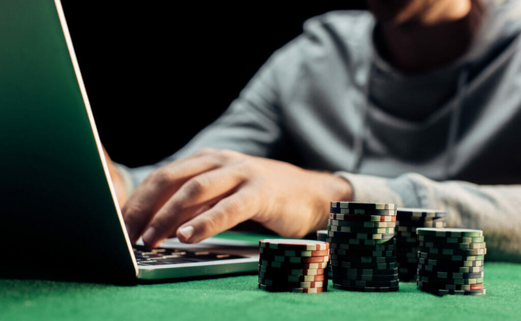 A close-up of a person typing on a laptop with poker chips next to them.