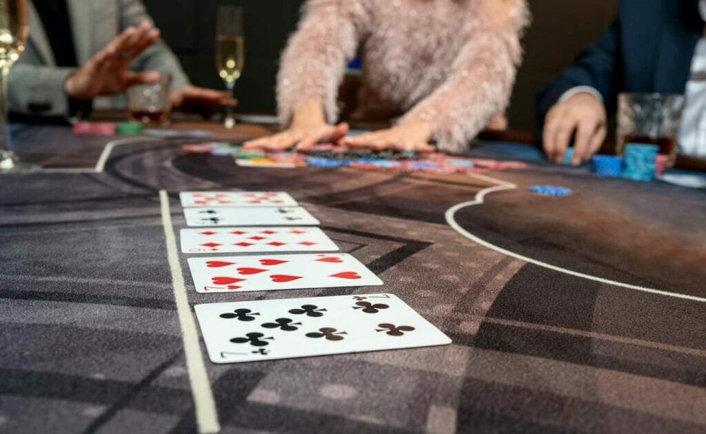 Five cards on a poker table with players in the background.
