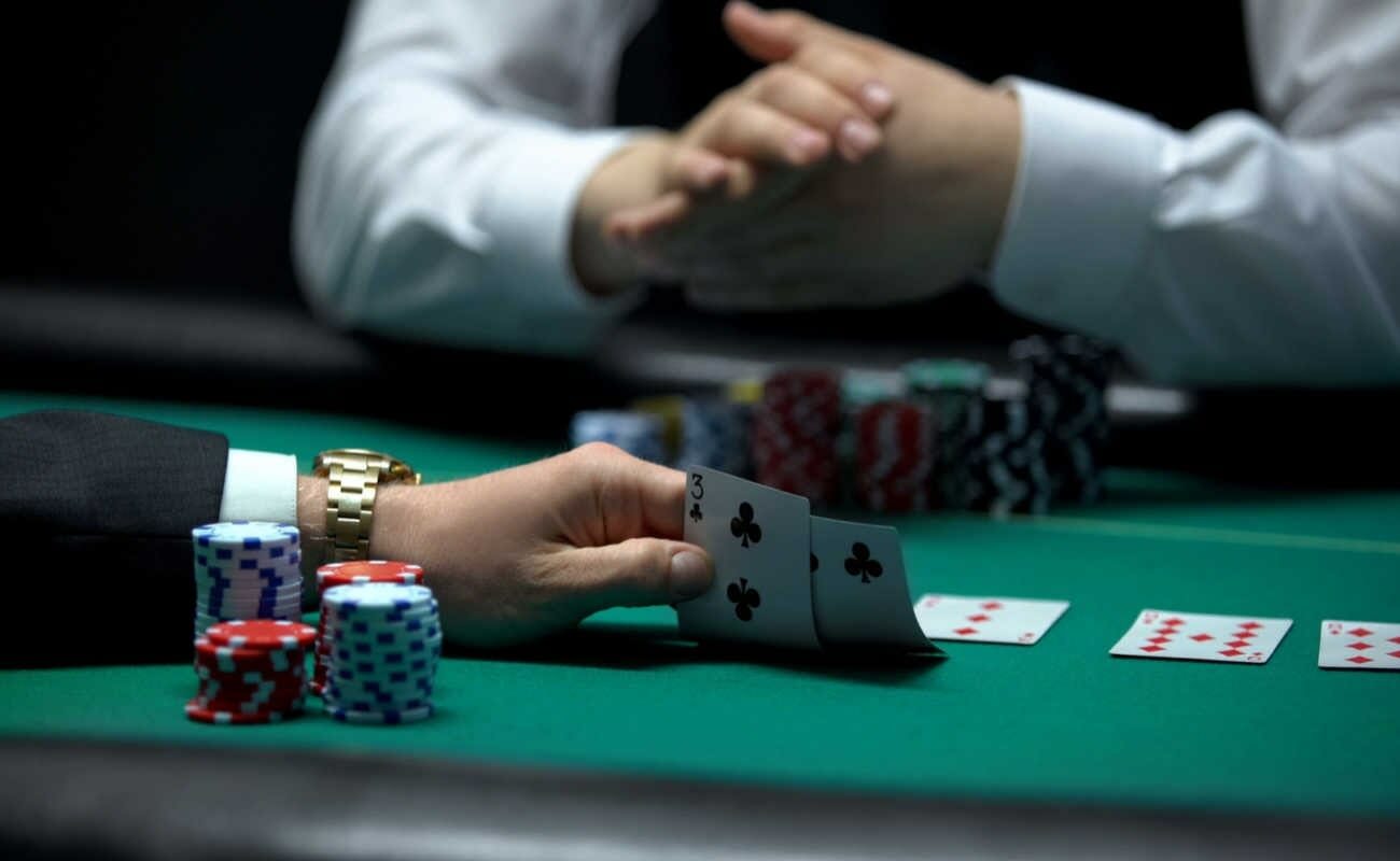 A man at a green poker table holding up two playing cards behind a stack of casino chips.