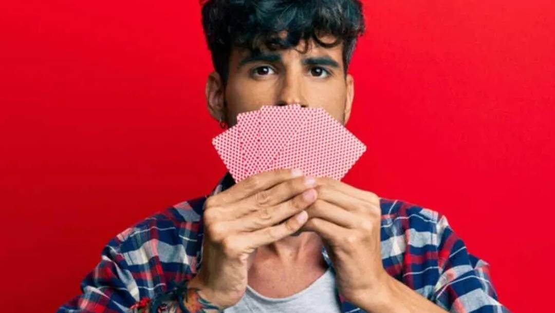 A man holds his hand of cards in front of his face.