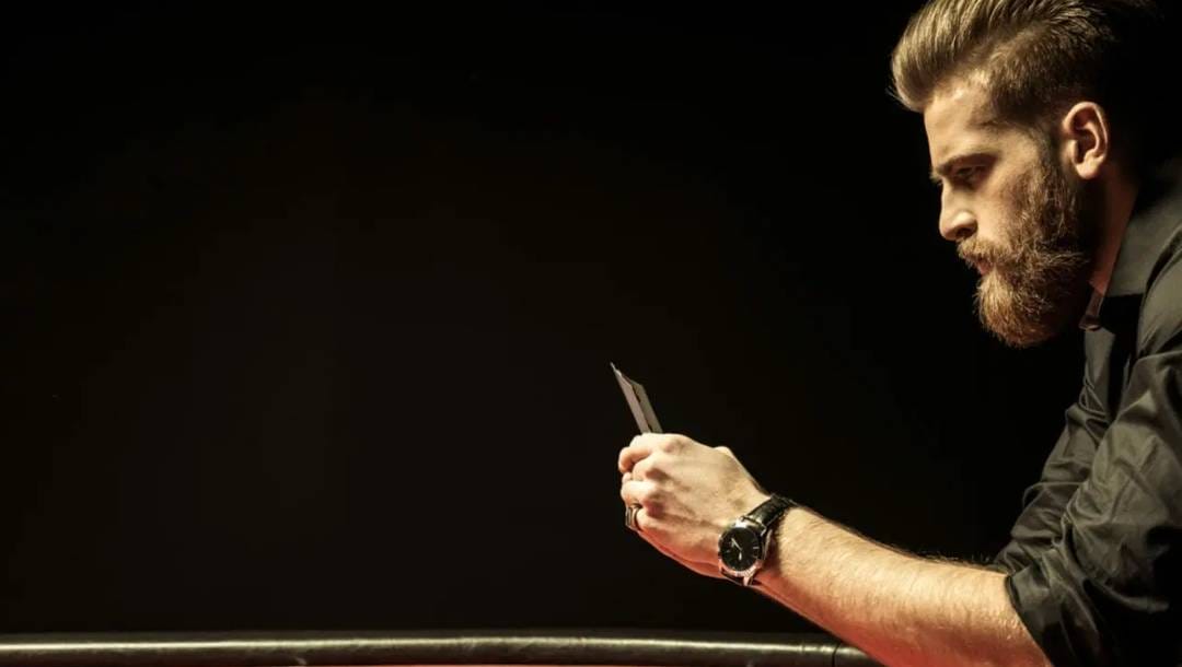 A side-on view of a man holding his poker hand up and looking at his cards.