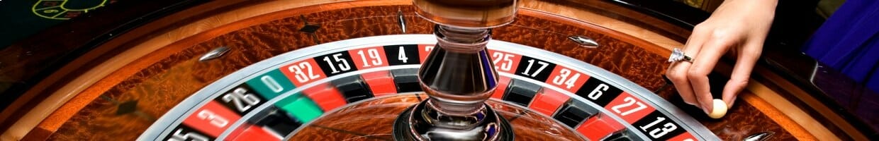 A close-up of a roulette wheel with the dealer about to drop the roulette ball into play.