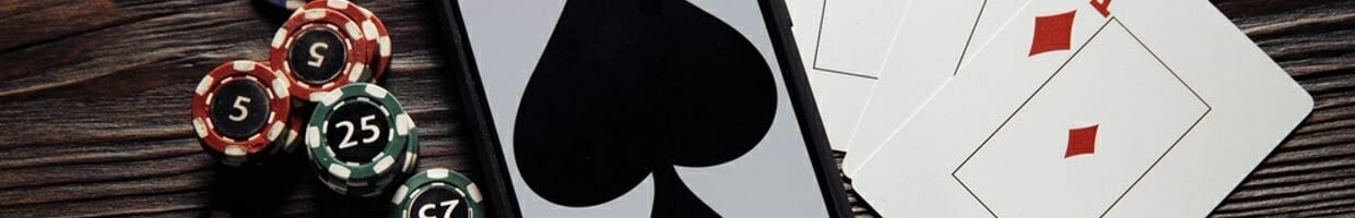 Playing cards and casino chips on either side of a smartphone that displays a spade.