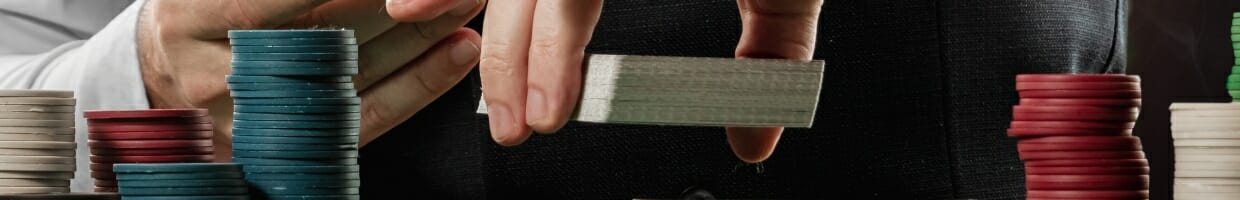 A croupier holding a deck of cards with poker chips in frame.
