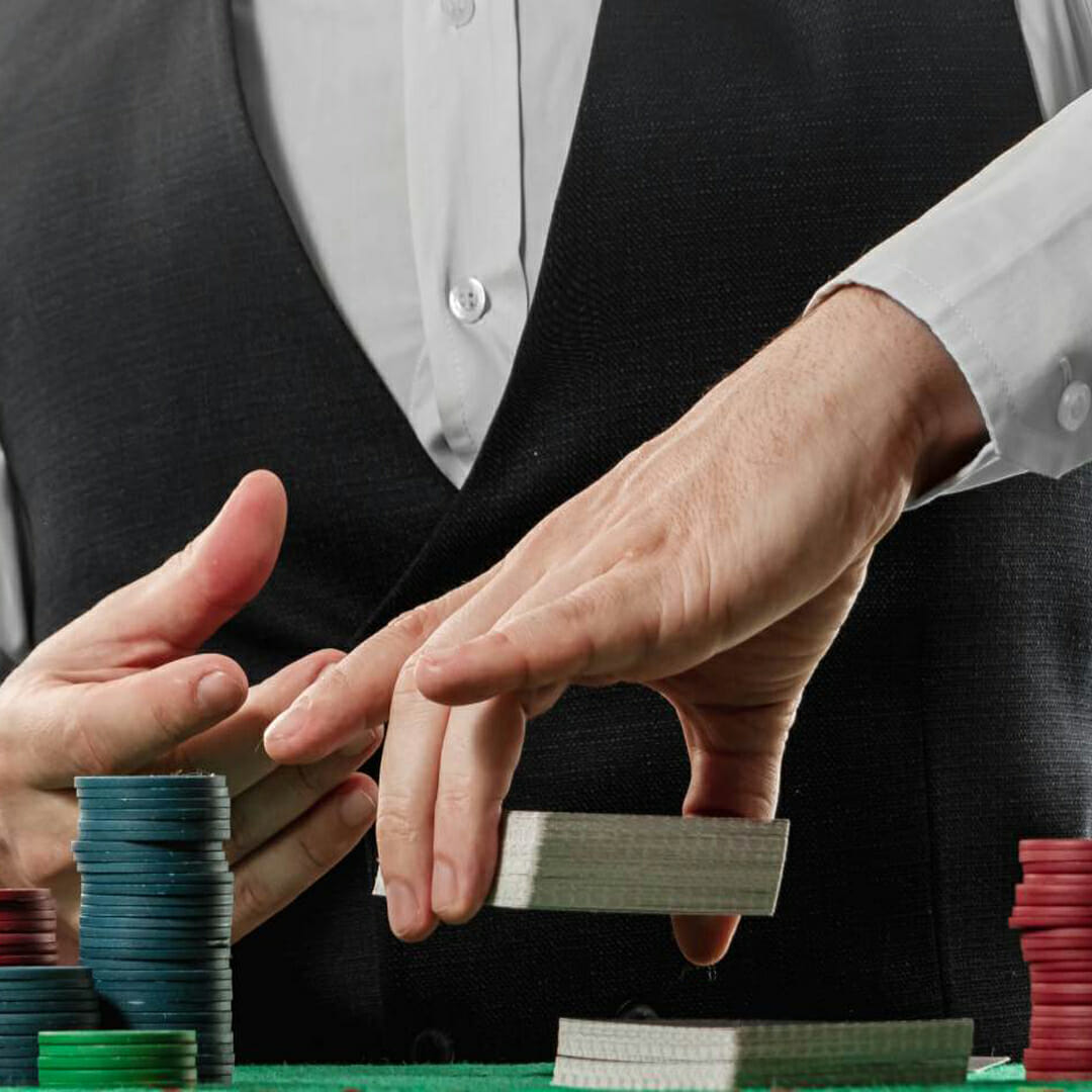 A croupier holding a deck of cards with poker chips in frame.