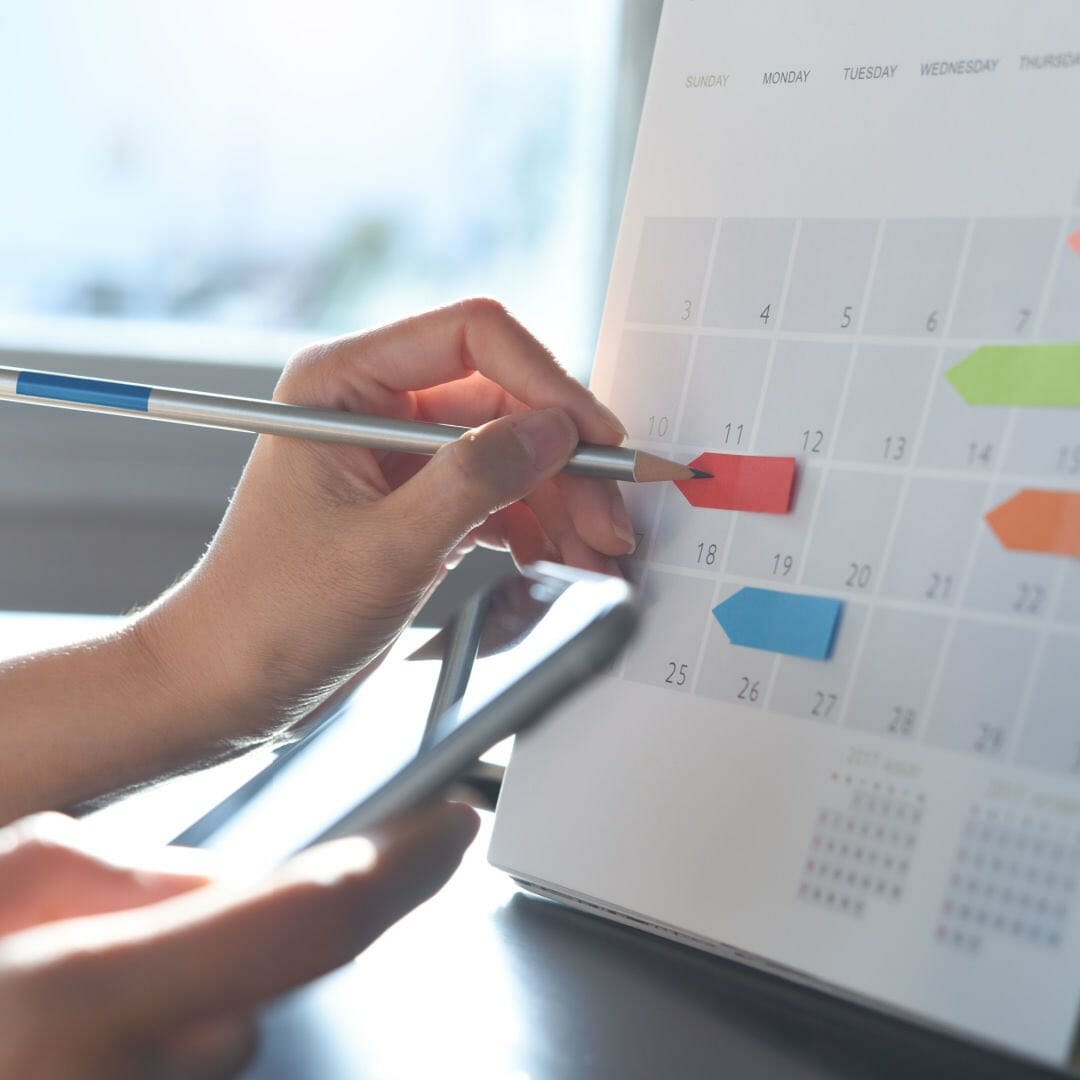 A person uses a pencil, smartphone and sticky notes to organize a calendar