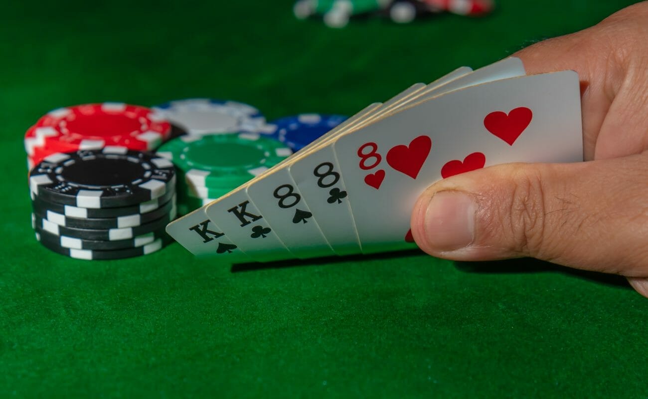 A poker player checks his five cards in a game of poker. He has a full house which is made up of two kings and three eights.