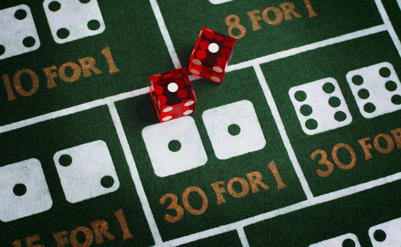 A pair of dice with “snake eyes” (two ones) facing up. These dice sit on a craps table with various dice odds on display.