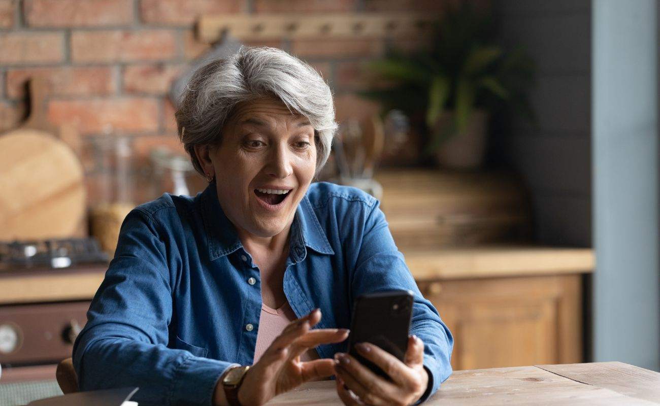 a woman is celebrating while sitting at a table and holding a cellphone and playing online casino games 