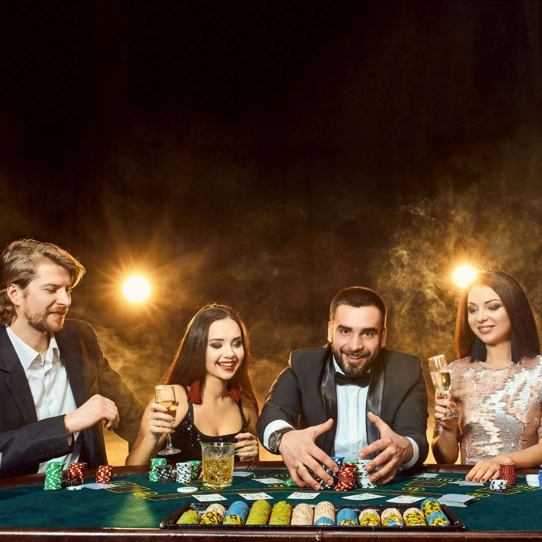 four people are sitting at a poker table in a casino and the one man pulls stacks of poker chips towards himself after winning