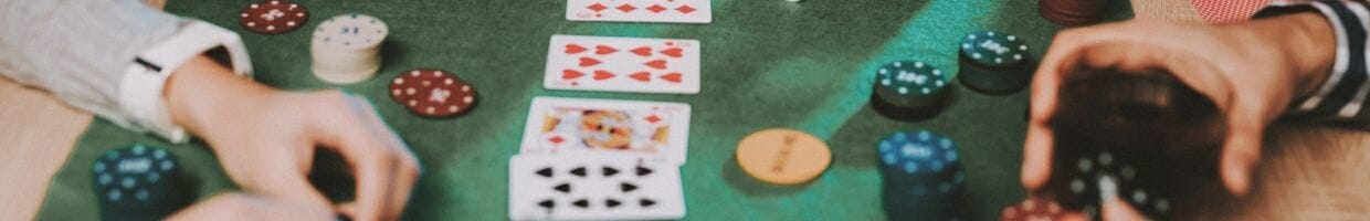 close up of an at-home poker game table with friends, there are playing cards, poker chips, a dealer token and player hands on the table