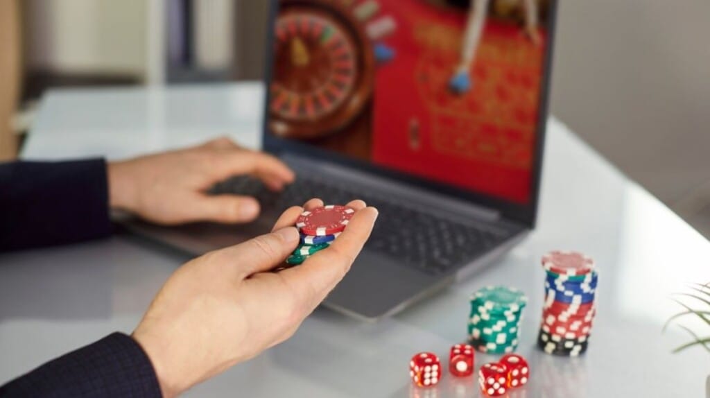 Person playing online roulette on a laptop while holding casino chips.