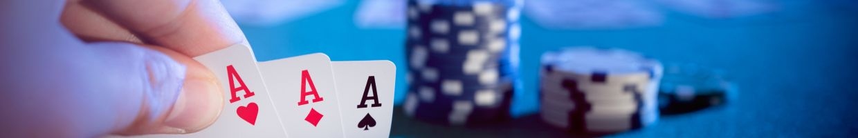 three of a kind ace playing cards on a blue felt poker table with poker chips in the background 