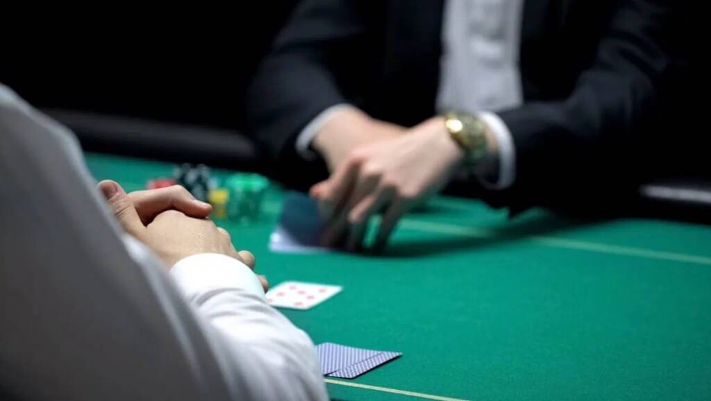 A poker player sitting with his hands together at a poker player while the player across from him checks their cards.