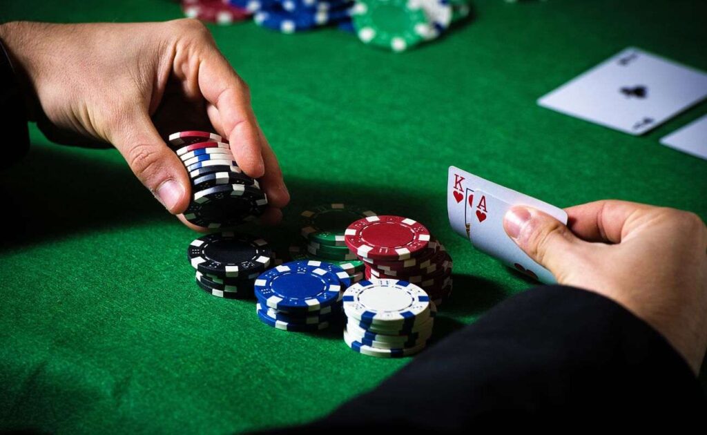 a close up of a person checking their hole cards, an ace and king of hearts, and picking up from a stack of poker chips on a green felt poker table 