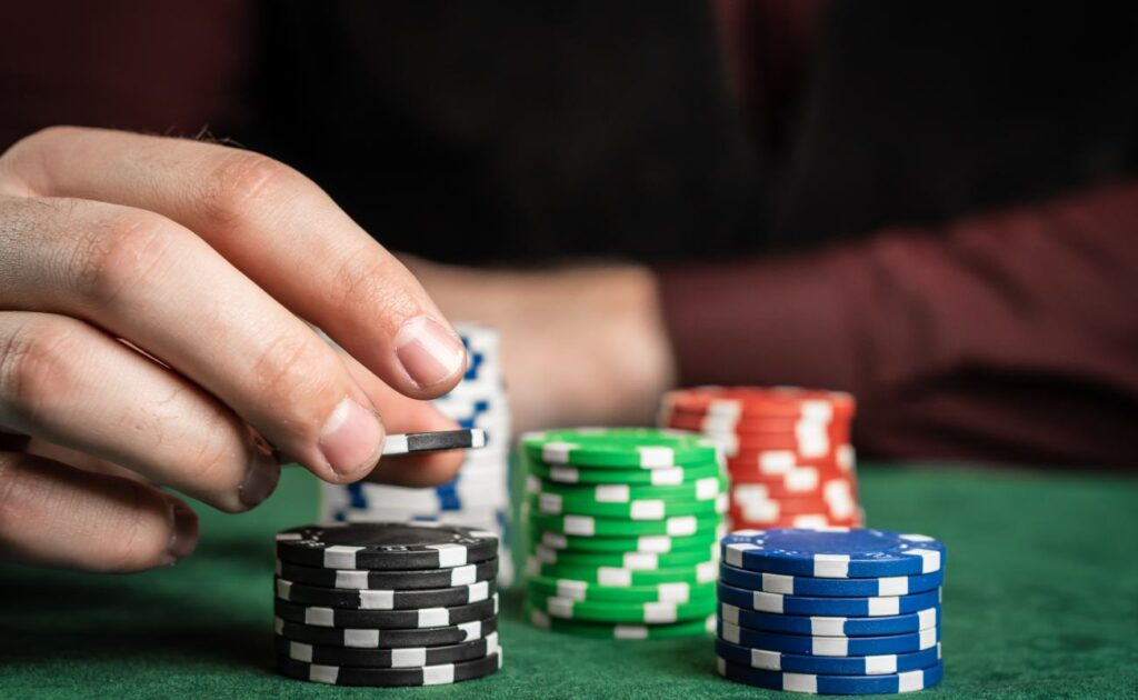A player picks up a black and white poker chip from a stack of chips. There are other colored poker chips on the game table.