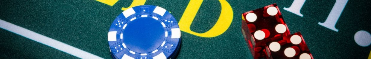 A close up of a blue casino chip, and two red dice on a craps table. 