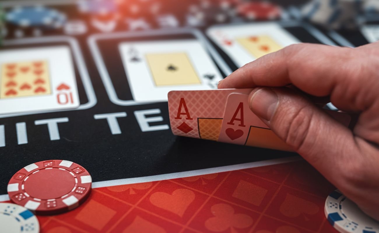 A person revealing an Ace of Hearts, and an Ace of diamonds, at a poker table, with poker chips and other playing cards arranged on the table. 