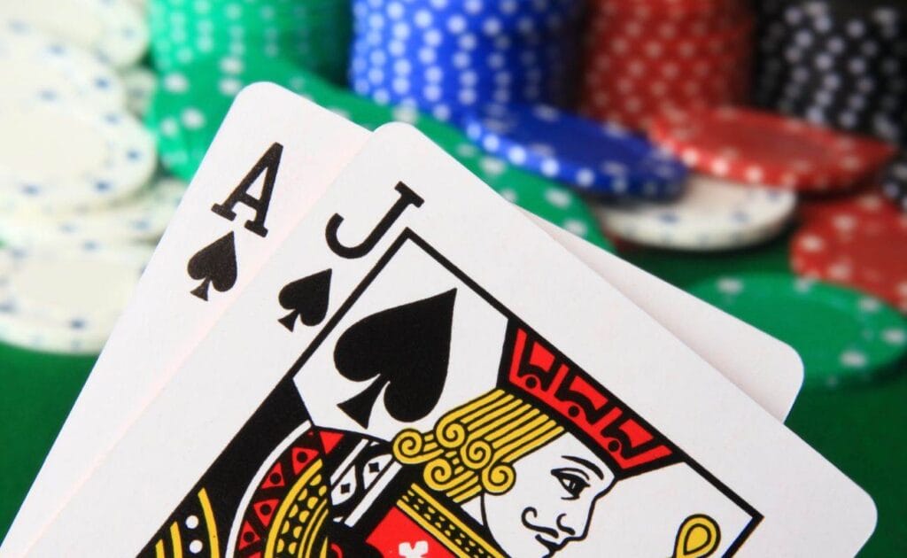 an ace and jack of spades playing cards held up in front of a green felt poker table with different colored poker chips stacked on it