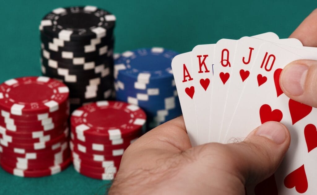 A poker player holding a royal flush. There are stacks of poker chips on the table behind his hand.