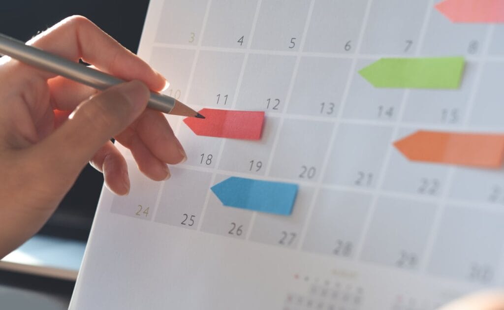 A person about to write on a paper calendar using a pencil.
