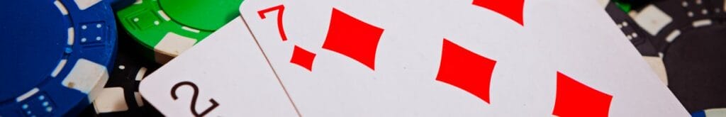 A 2 of spades and a 7 of diamonds on top of scattered, black, blue, and green poker chips.