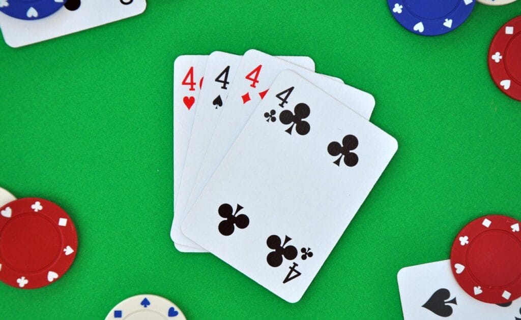 Four 4s on a casino table surrounded by scattered poker chips and cards.