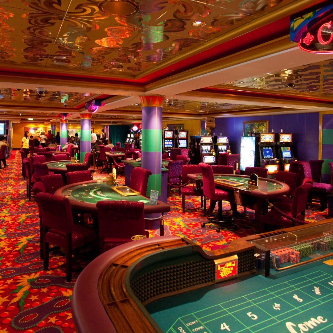 The inside of a casino with casino table games and slot machines.