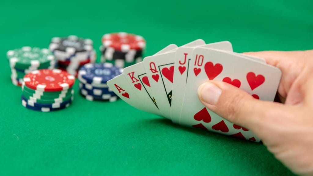 A poker player peaks at their cards. They have a royal flush. Stacks of poker chips are visible in the background.