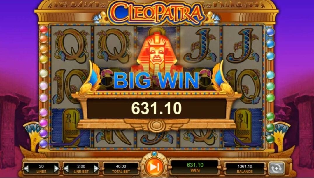 A screenshot of a Big Win in the Cleopatra slot game. In the foreground is a notification of a payout of 631.10. It’s prominently featured in the center of the screen. The announcement appears beneath a glowing golden pharaoh mask, flanked by Egyptian wings and framed in a stylized wooden panel. Behind this, the five-reel slot layout remains partially visible, filled with Egyptian-themed symbols, like the Eye of Horus, gold plaques, and card values. The background has a gradient sky in deep purple transitioning to pink, accompanied by faded sandstone pillars. Below the reels is the game interface.
