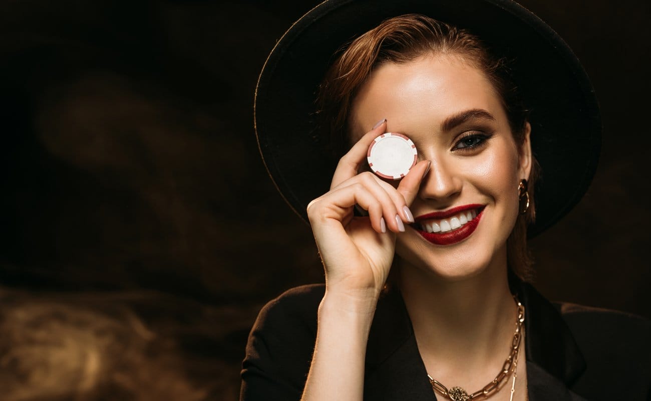 A poker player holds a poker chip up in front of their right eye.