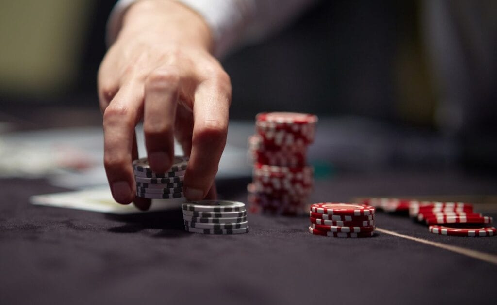 Person placing a stack of poker chips on to a black felt table.