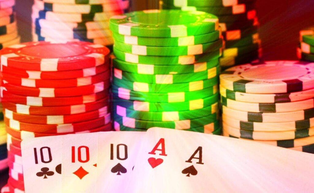 A ten of Clubs, a ten of Diamonds, a ten of Spaces, an Ace of Hearts, and an Ace of Spades arranged in front of stacks of poker chips.