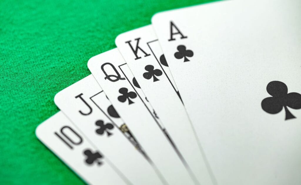 A ten of Clubs, a Jack of Clubs, a Queen of Clubs, a King of Clubs, and an Ace of Clubs, arranged on a poker table. 