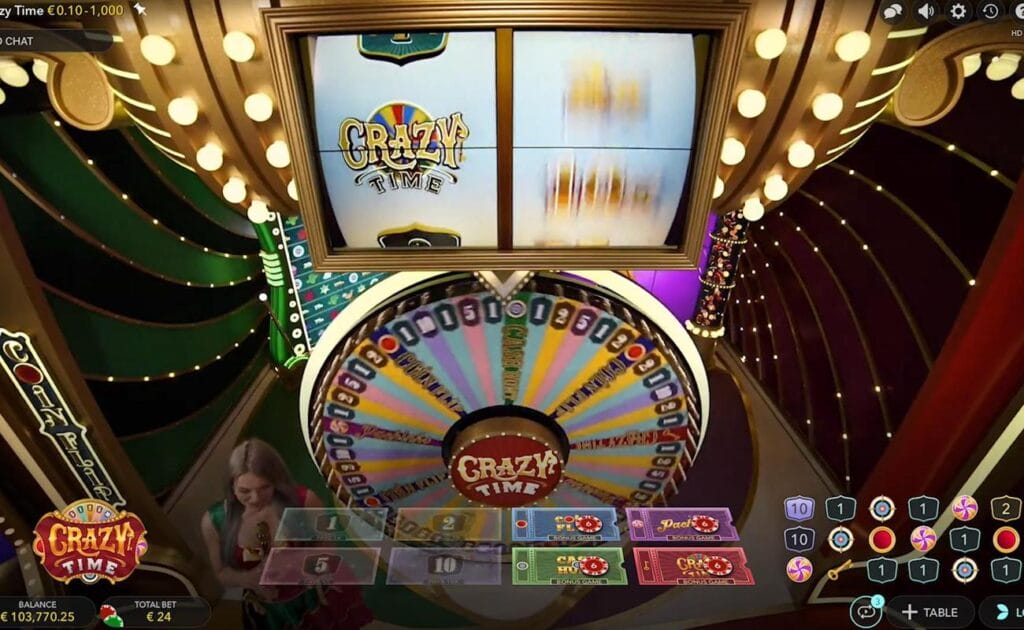 The gameplay in Crazy Time from the Evolution promotional video. The camera is focused on the top slot as it spins, with the wheel spinning below it. The host stands on the left side next to the wheel.