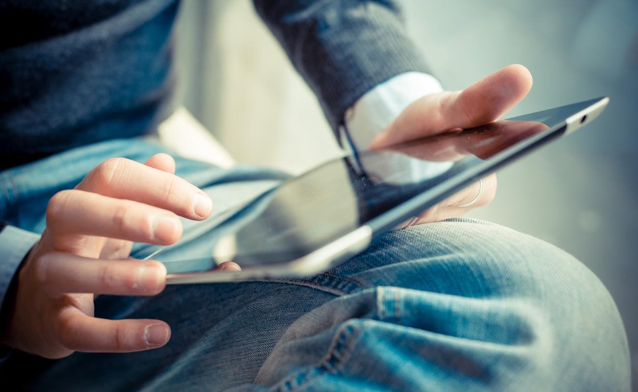 A close up of a person sitting and reading a tablet while sitting with their leg over one knee.