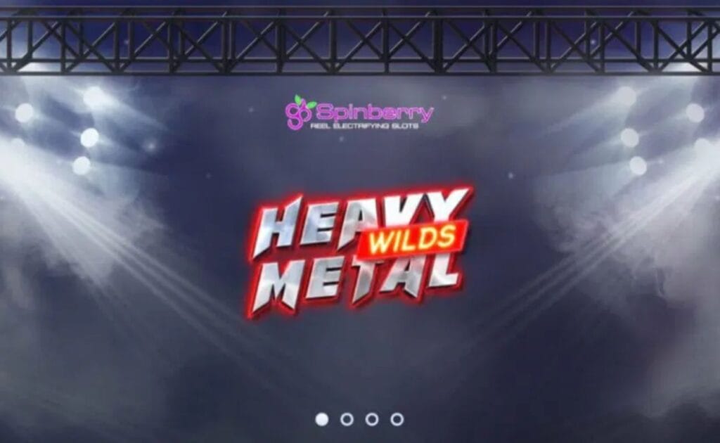 A screenshot of the Heavy Metal Wilds logo in a classic metal-style font floating on top of  a dark, foggy stage lit by spotlights with the Spinberry logo and a stage truss running along the top of the image. 