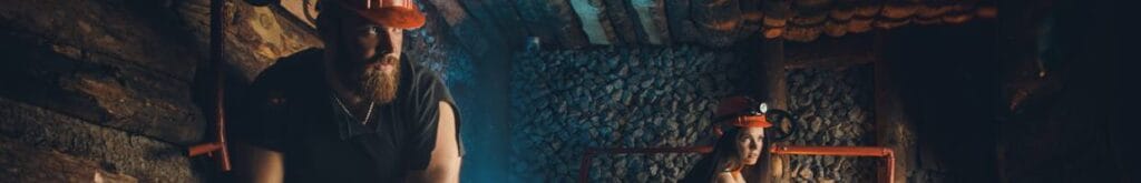 Two miners in orange hardhats working in a mine.