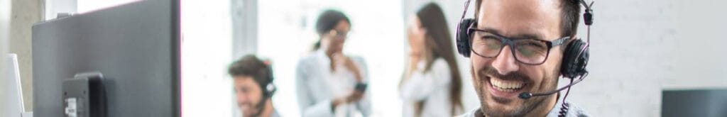 A smiling customer support agent sitting at his desk in front of his computer.